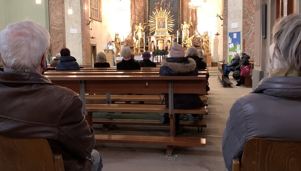 Gläubige in der Kirche mit Sicherheitsabstand und Maske
