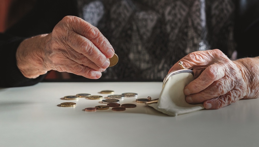 Elderly 95 years old woman sitting miserably at the table at home and counting remaining coins from the pension in her wallet after paying the bills.